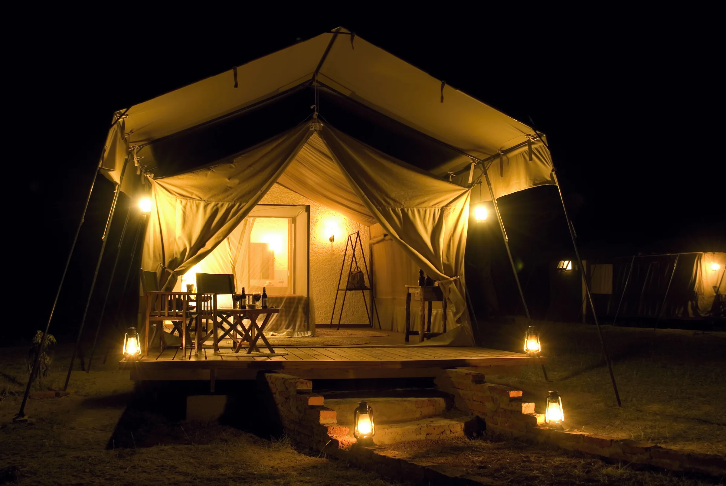 A luxury safari tent at Nsya Lodge lit by lanterns after dark