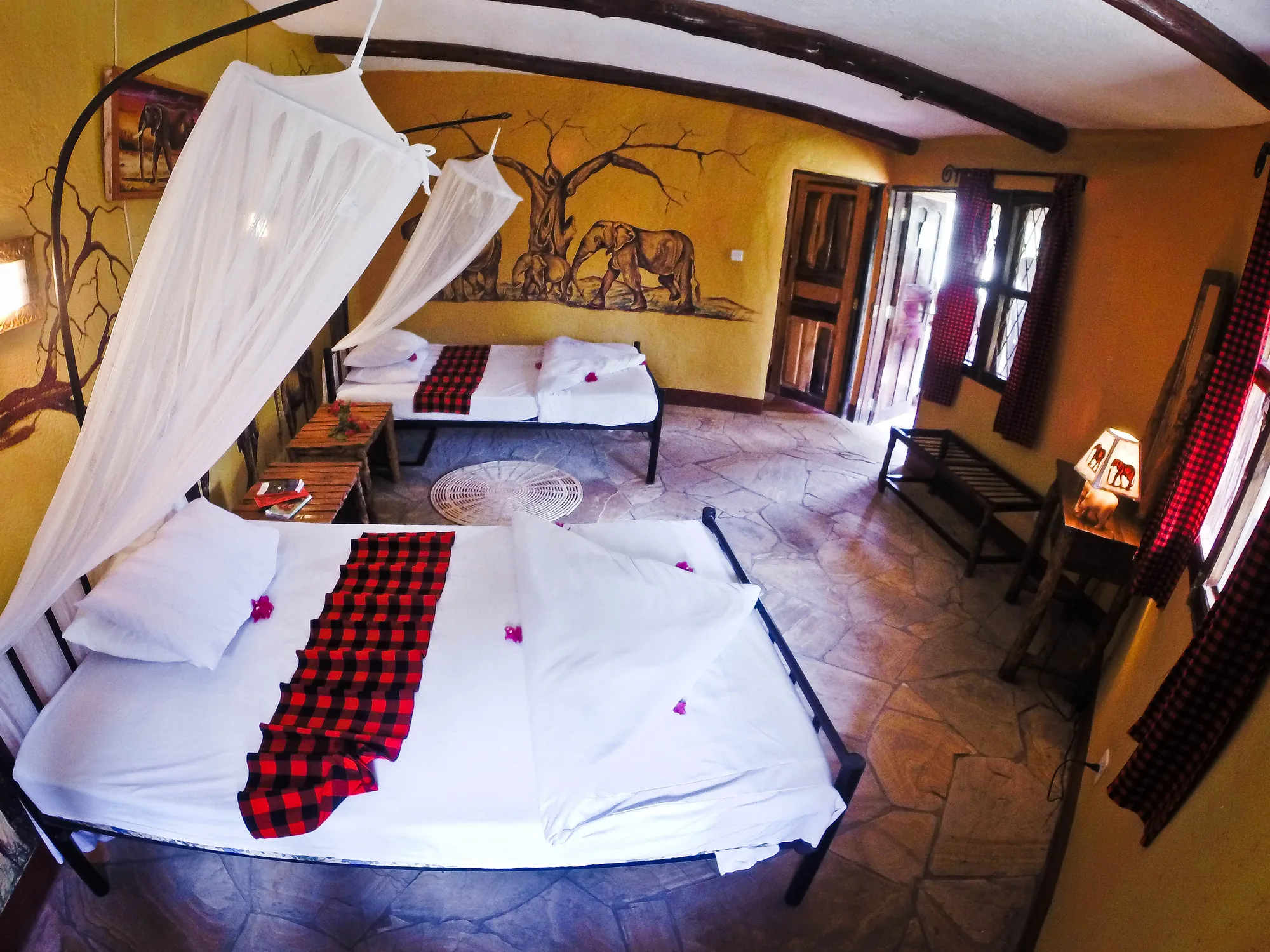 A triple cottage room with a double and a single bed, and an elephant mural on the ochre wall